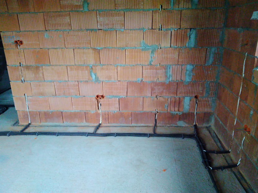 Surowa ściana z czerwonej cegły z widocznymi, nowo poprowadzonymi przewodami elektrycznymi w peszlach i puszkach instalacyjnych, przygotowana do dalszych prac wykończeniowych.