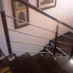 Nowoczesna poręcz schodowa z drewnianymi słupkami, metalowymi prętami i srebrnymi mocowaniami. Schody wykończone ciemnym drewnem.