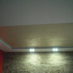 Oświetlony sufit podwieszany z dekoracyjną fakturą, wkomponowany w aranżację wnętrza z akcentem na kamienną ścianę i oświetlenie punktowe.