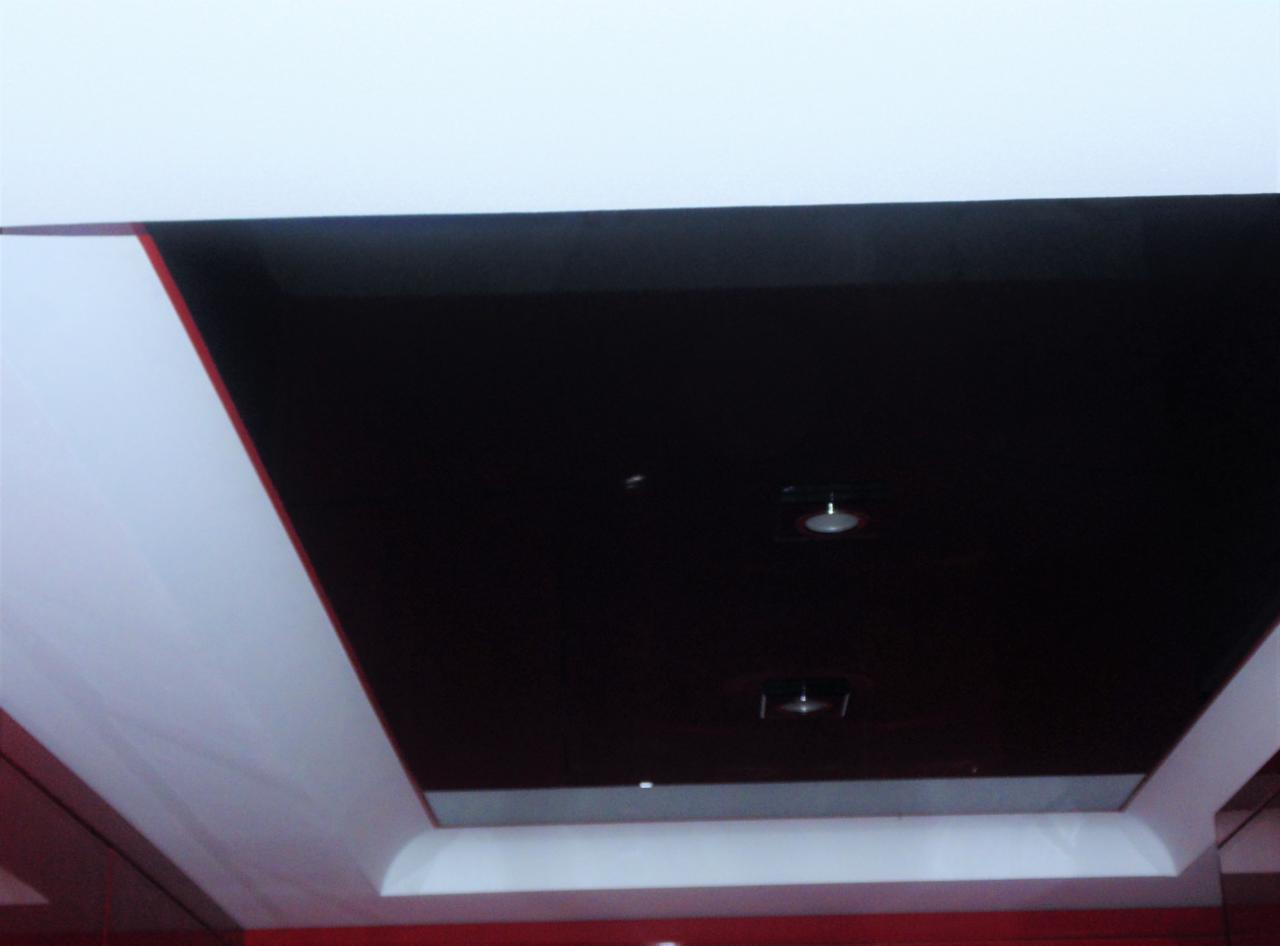 Błyszczący, czarny sufit podwieszany z dwoma punktowymi lampami LED, otoczony białym obramowaniem z czerwonym akcentem, widziany pod kątem.