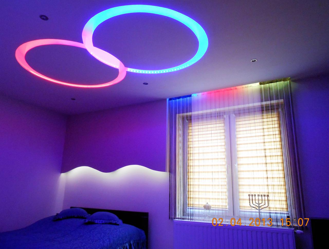 Nowoczesny pokój z podwieszanym sufitem z oświetleniem LED w kształcie dwóch przenikających się okręgów. Kolorowe światło podkreśla aranżację wnętrza.