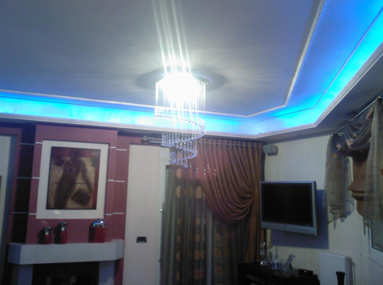Salon z podwieszanym sufitem z niebieskim oświetleniem LED, spiralnym żyrandolem i dekoracyjnymi zasłonami. Widoczny fragment ściany z obrazem.