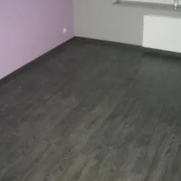 Ukończona podłoga z ciemnych paneli w pokoju z fioletową i szarą ścianą. Widoczny grzejnik pod oknem. Podłoga z wyraźną strukturą drewna.