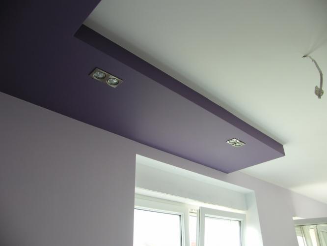 Fioletowy sufit podwieszany z oświetleniem punktowym w nowoczesnym wnętrzu, widok z dołu, jasne ściany, okno z białymi ramami.