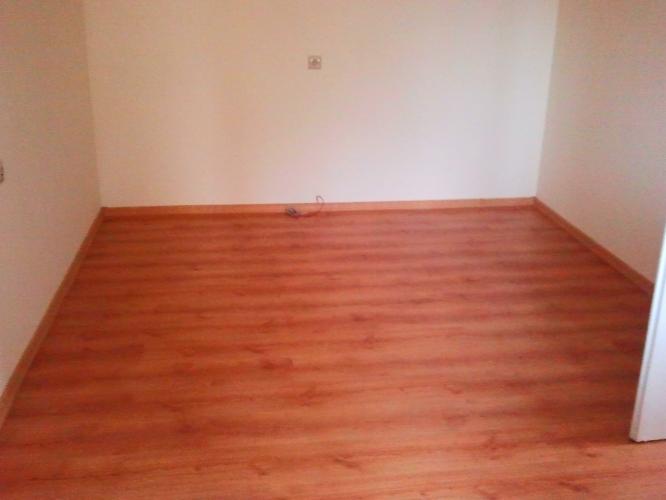 Pokój po ułożeniu paneli podłogowych w odcieniach brązu. Widoczne ściany pomalowane na biało i gniazdko elektryczne. Kąt ujęcia podkreśla nową podłogę.