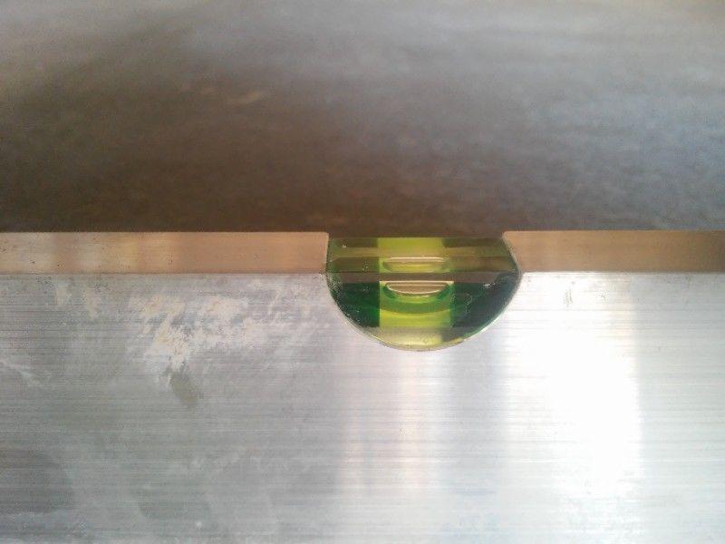 Poziomica na metalowej powierzchni. Libella wskazuje poziom, co sugeruje precyzyjne prace budowlane.