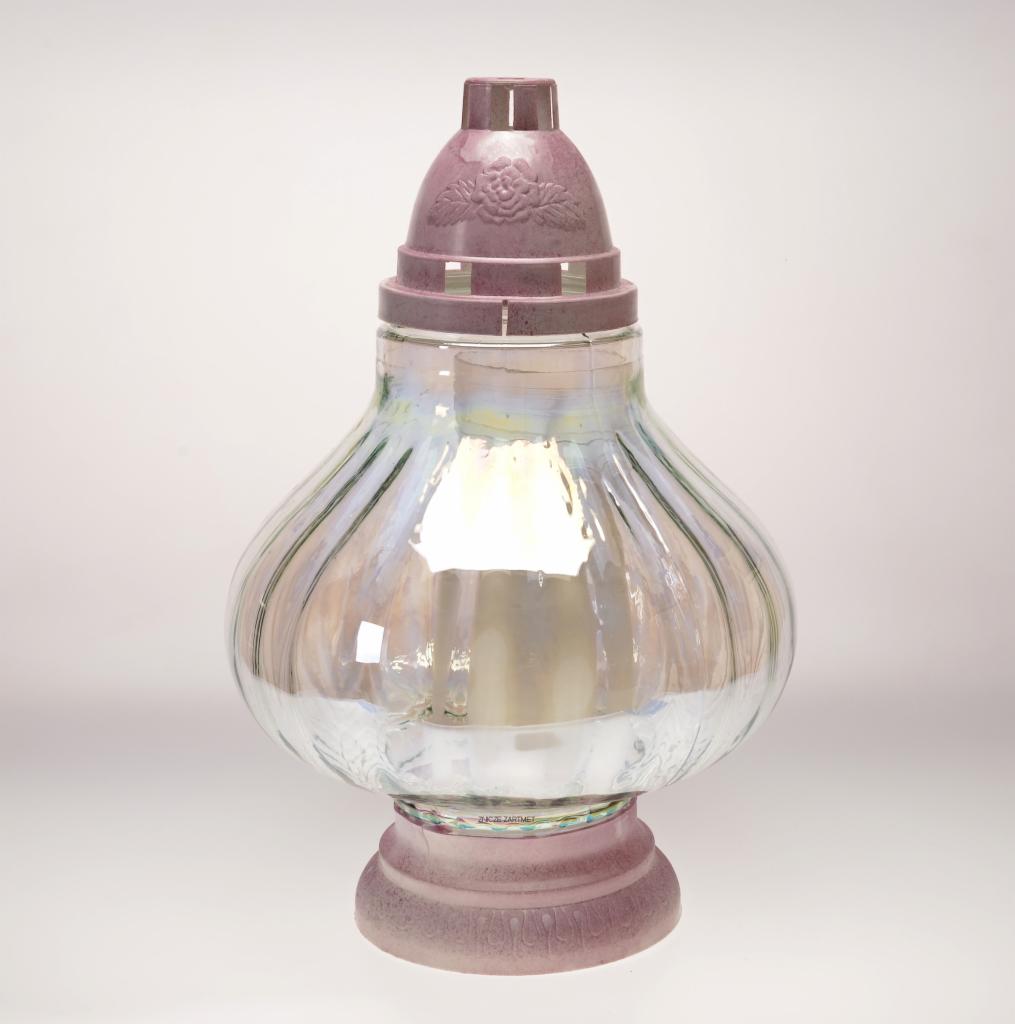 Szklany znicz w odcieniach różu i iryzacji. Na podstawie i z pokrywką z motywem róży. Widoczne pionowe żłobienia na szkle. Subtelne światło wewnątrz.