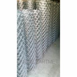 Zrolowana, ocynkowana siatka ogrodzeniowa z widocznym logo producenta, ustawiona w pionie na betonowej posadzce. Widoczne oczka siatki w kształcie rombów.