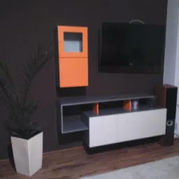 Nowoczesna aranżacja salonu z wiszącą szafką RTV, pomarańczową szafką i telewizorem na brązowej ścianie. Uzupełnieniem jest roślina w białej donicy.