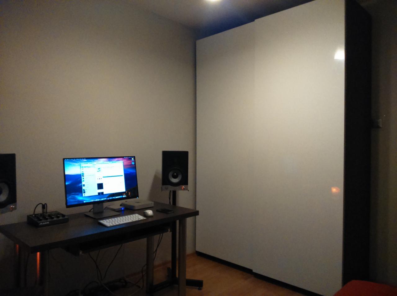 Biała szafa przesuwna w pokoju z biurkiem i sprzętem audio. Minimalistyczny design, ciemne obramowanie szafy i jasne fronty. Dobre oświetlenie.