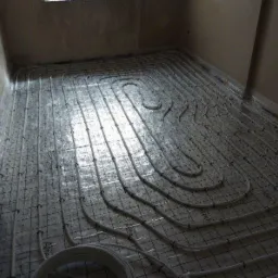 Białe rury ogrzewania podłogowego ułożone na siatce, gotowe do zalania posadzką. Widoczne detale mocowań i etykiety producenta na folii zabezpieczającej.