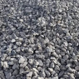 Kupa szarego tłucznia na placu składowym, widoczne drzewa w tle.