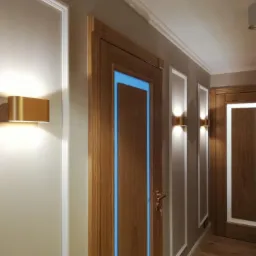 Korytarz z drewnianymi drzwiami z podświetleniem LED w kolorze niebieskim, oświetlony złotymi lampami ściennymi i wykończony listwami dekoracyjnymi