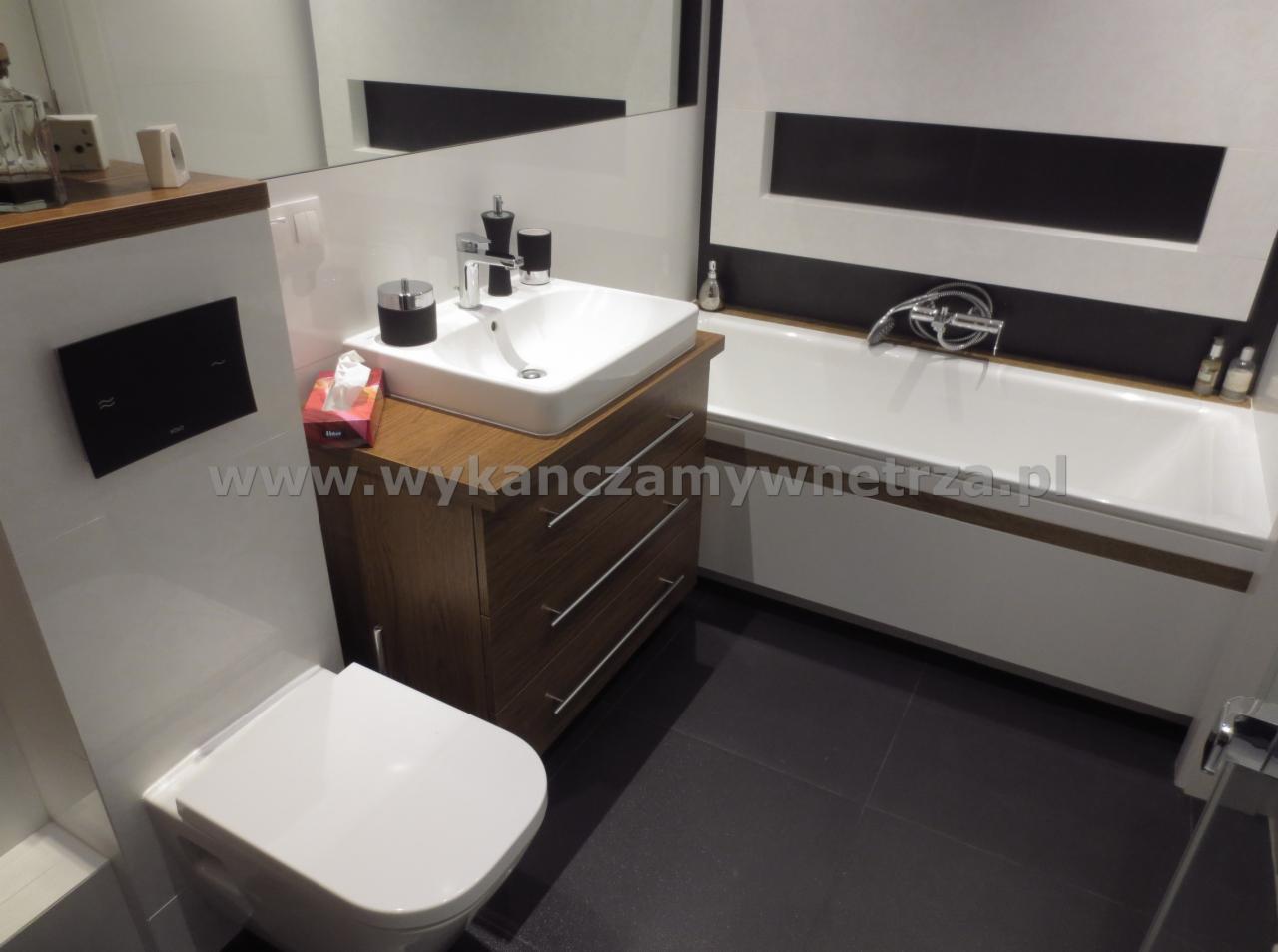 Nowoczesna łazienka: biała ceramika, drewniana szafka pod umywalką, czarne płytki podłogowe. Minimalistyczny design, czyste linie, wanna z hydromasażem.