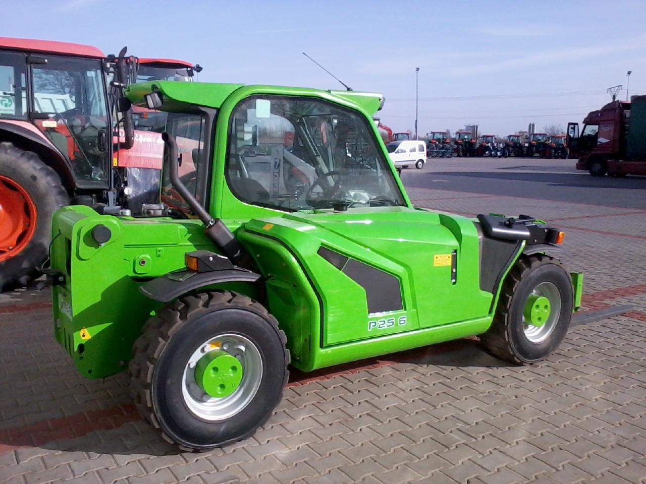 Zielona ładowarka teleskopowa P25.6 na brukowanym placu, z widocznymi innymi pojazdami w tle. Jasne niebo i dobre oświetlenie podkreślają detale maszyny.