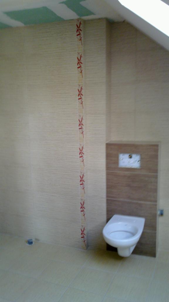 Wykończona łazienka z beżowymi płytkami imitującymi drewno, ozdobnym pionowym pasem z czerwonym wzorem i podwieszaną toaletą na brązowym panelu.