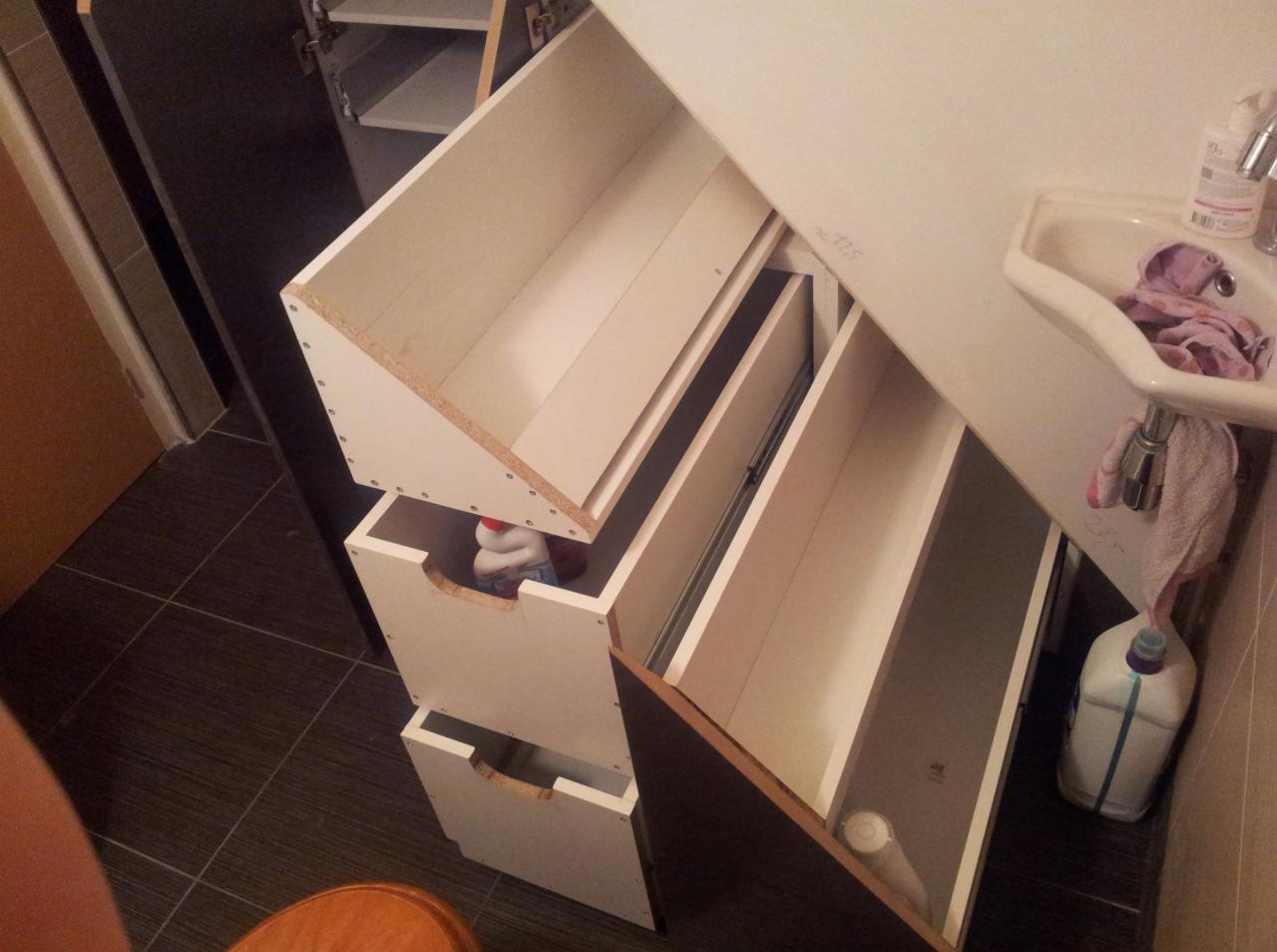 Otwarta szafka łazienkowa z wysuniętymi szufladami, widoczna umywalka i akcesoria. Ujęcie z góry, ukazujące wnętrze szafki i jej zawartość.