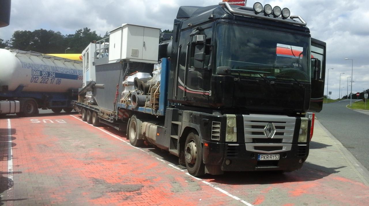 Czarna ciężarówka Renault Magnum z naczepą przewożąca ładunek, zaparkowana na czerwonym pasie postojowym z napisem BUS. Widoczna inna ciężarówka w tle.