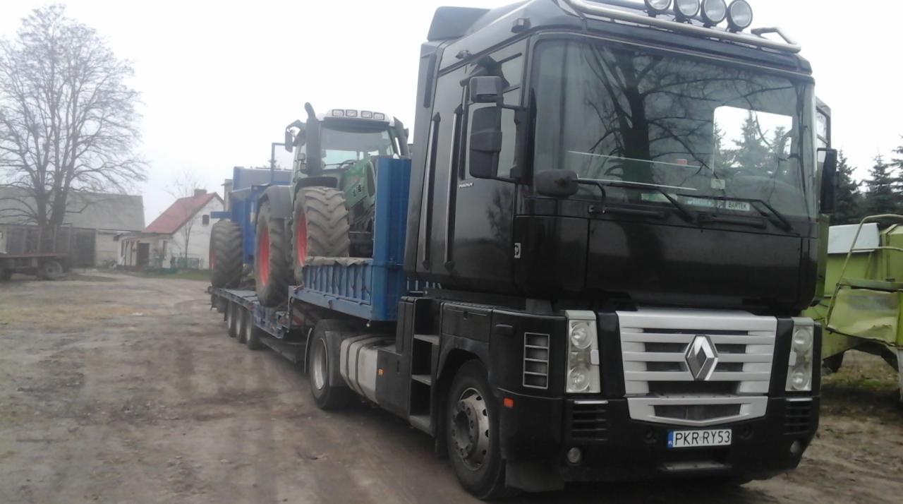Czarny ciągnik siodłowy Renault z naczepą niskopodwoziową przewozi traktor rolniczy na tle wiejskiego krajobrazu w pochmurny dzień.