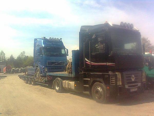 Czarna laweta Renault Magnum transportuje niebieskiego Volvo FH z kabiną sypialną, widoczne światła na dachu i tablice rejestracyjne.