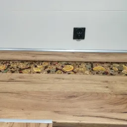 Blat kuchenny z żywicą epoksydową, w której zatopione są suszone pomarańcze, przyprawy i liście laurowe, podświetlony od góry, z widocznym gniazdkiem elektrycznym na ścianie.