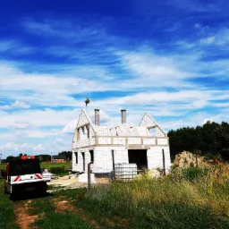 Stan surowy otwarty domu jednorodzinnego z białego bloczka, widok z poziomu gruntu, na pierwszym planie dostawczy samoch&oacute;d budowlany