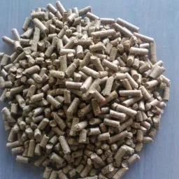 Stos brązowych peletów drzewnych na niebieskim tle, widoczne nierówności i drobne pęknięcia na powierzchni peletów.