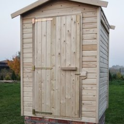 Marcin Pląskowski - Drewniana budka narzędziowa na fundamencie z cegieł, z metalowymi zawiasami, w Starogardzie Gdańskim. Solidna konstrukcja, widoczne usłojenie drewna.