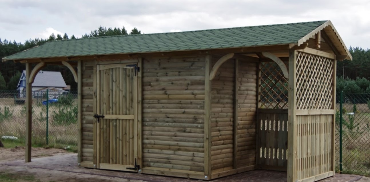 Drewniana konstrukcja z zielonym dachem, zamykana drzwiami i ozdobną kratką, w tle drzewa i dom. Widoczna precyzja wykonania i dbałość o detale.