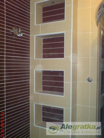 Beżowo-brązowa łazienka z wnękami wyłożonymi płytkami, widoczny prysznic i bateria. Ułożenie płytek w poziome pasy. Wykończenie wnęk w jasnym odcieniu beżu.