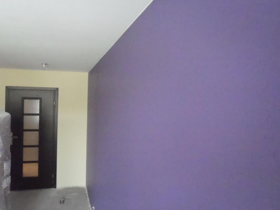 Pomieszczenie po malowaniu ścian na fioletowo, widoczna czarna, przeszklona rama drzwiowa i fragment ściany w kolorze kremowym.