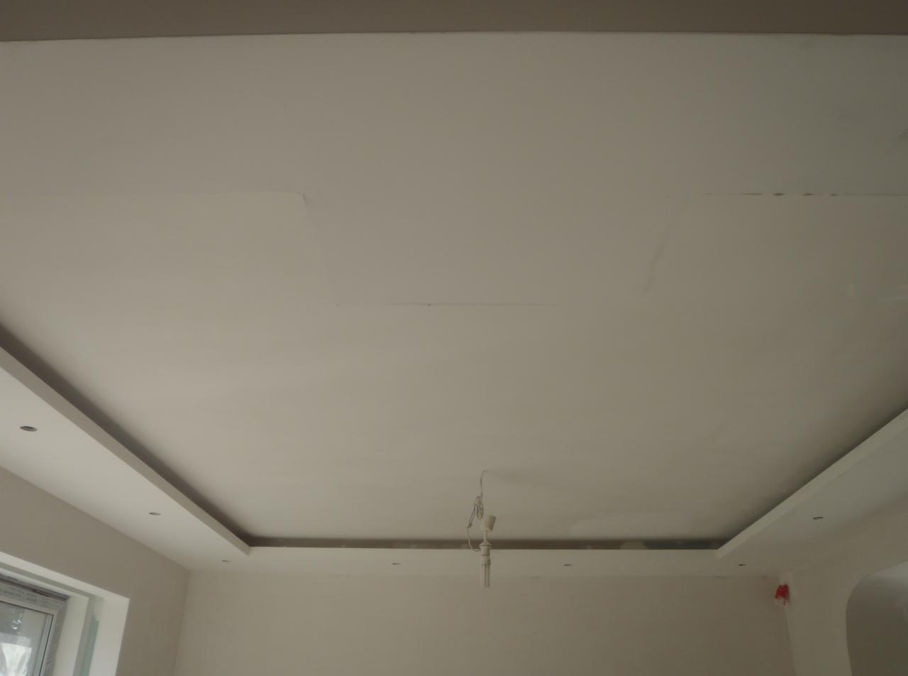 Wykończony sufit podwieszany z oświetleniem punktowym w jasnym wnętrzu. Widoczne kable wystające z sufitu.