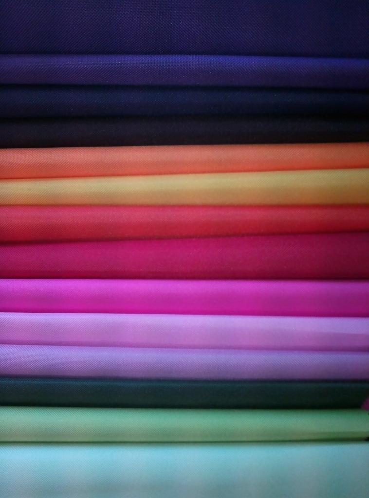 Paleta kolorowych tkanin ułożonych warstwami, prezentująca bogaty wybór materiałów w odcieniach fioletu, różu, pomarańczy i zieleni, idealnych do szycia.