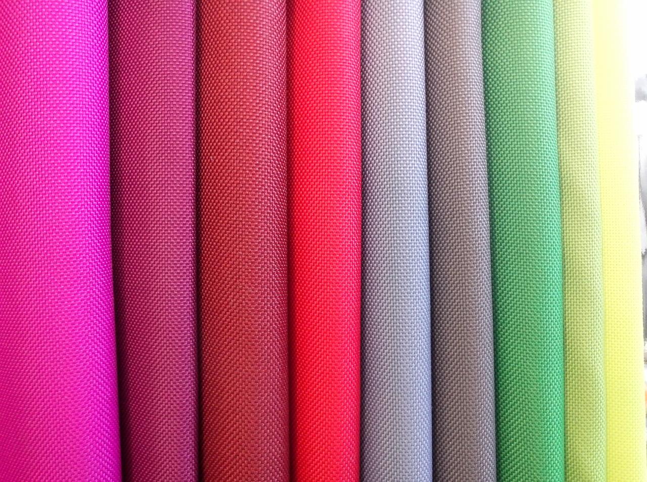 Paleta kolorów tkanin w rolkach o wyraźnej fakturze, od fuksji po jasnożółty, tworząca barwną kompozycję dla projektantów i producentów odzieży.