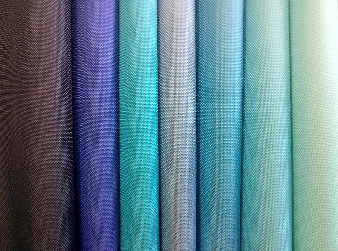 Paleta tkanin o zróżnicowanej teksturze i odcieniach: od ciemnego brązu, przez fiolety i błękity, aż po jasne turkusy i zielenie. Bliskie ujęcie prezentuje bogactwo kolorów.