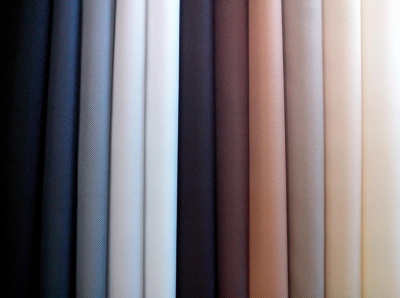 Próbki tkanin w różnych odcieniach, ułożone pionowo obok siebie. Widoczna faktura materiału i bogata paleta barw, od ciemnych po jasne beże.