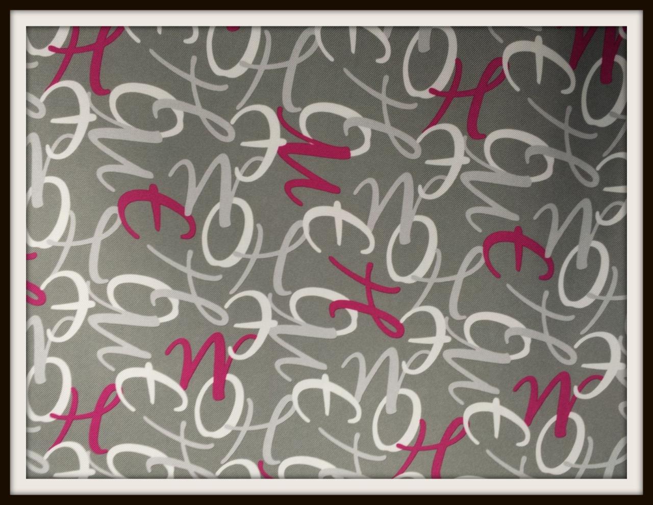 Szara tkanina z abstrakcyjnym, kaligraficznym wzorem w odcieniach bieli, szarości i fuksji. Wzór przypomina litery, tworząc dynamiczną i nowoczesną kompozycję.