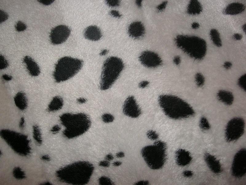 Biała tkanina pluszowa w czarne, nieregularne cętki, przypominająca wzór dalmatyńczyka, z widoczną fakturą materiału.
