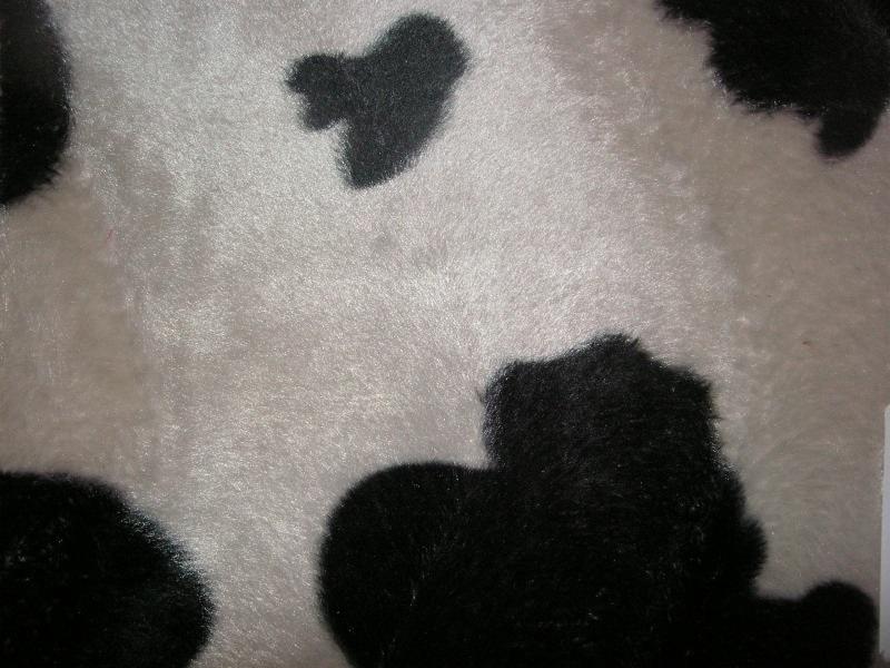 Czarno-biała, miękka tkanina imitująca wzór krowy, z widoczną fakturą futerka. Materiał o nieregularnych plamach, idealny na tekstylia domowe.