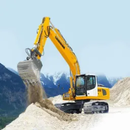 Żółta koparka Liebherr 916 nabiera ziemię na tle gór. Maszyna na gąsienicach wykonuje prace ziemne, widoczne świeże ślady. Jasne, naturalne oświetlenie.