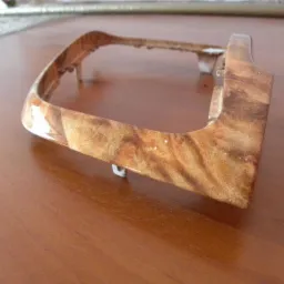 Drewnopodobna ramka, prawdopodobnie element wykończeniowy wnętrza, leży na drewnianym blacie. Widoczne detale imitacji drewna.