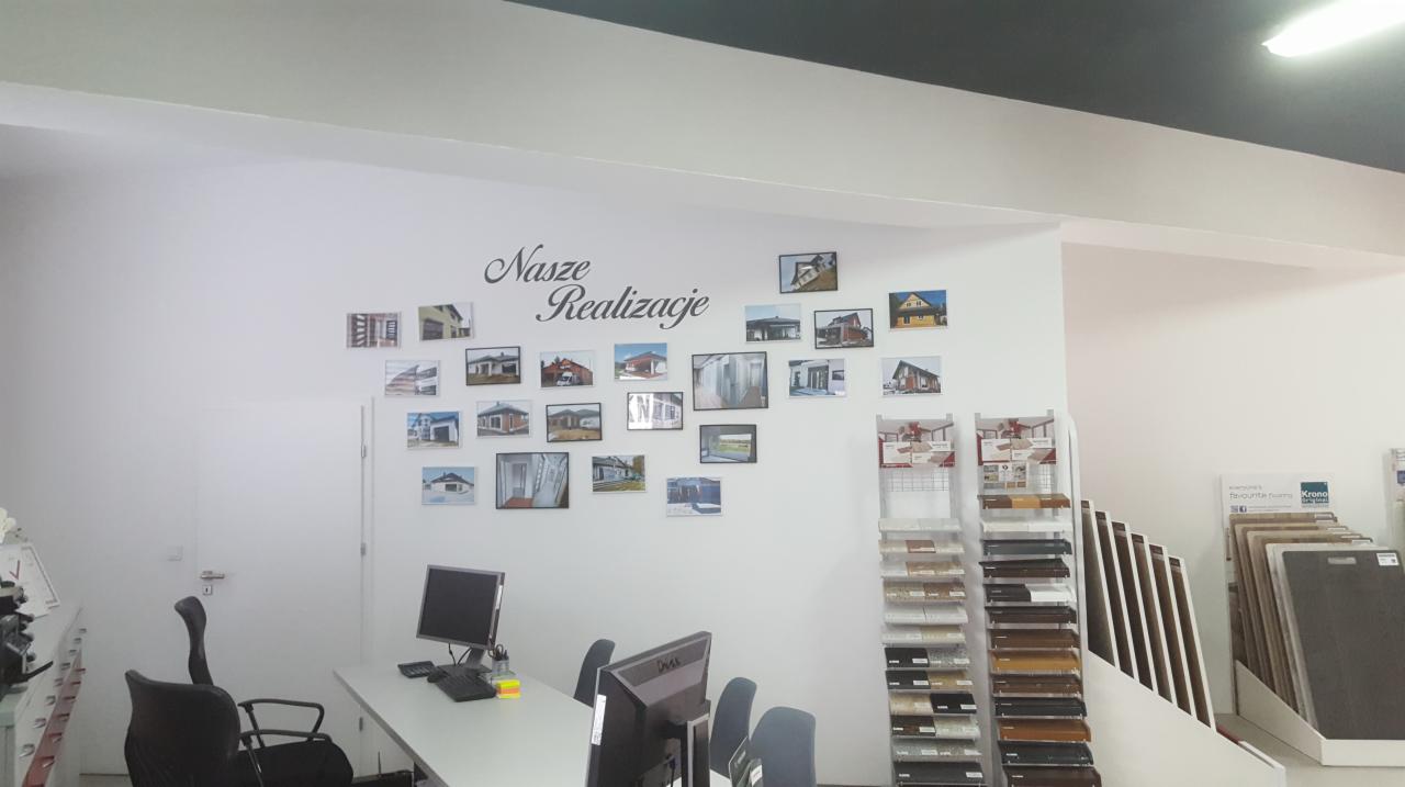 Wnętrze biura firmy EMKAT Radomsko z ekspozycją zdjęć realizacji na ścianie i próbkami materiałów budowlanych na regałach.