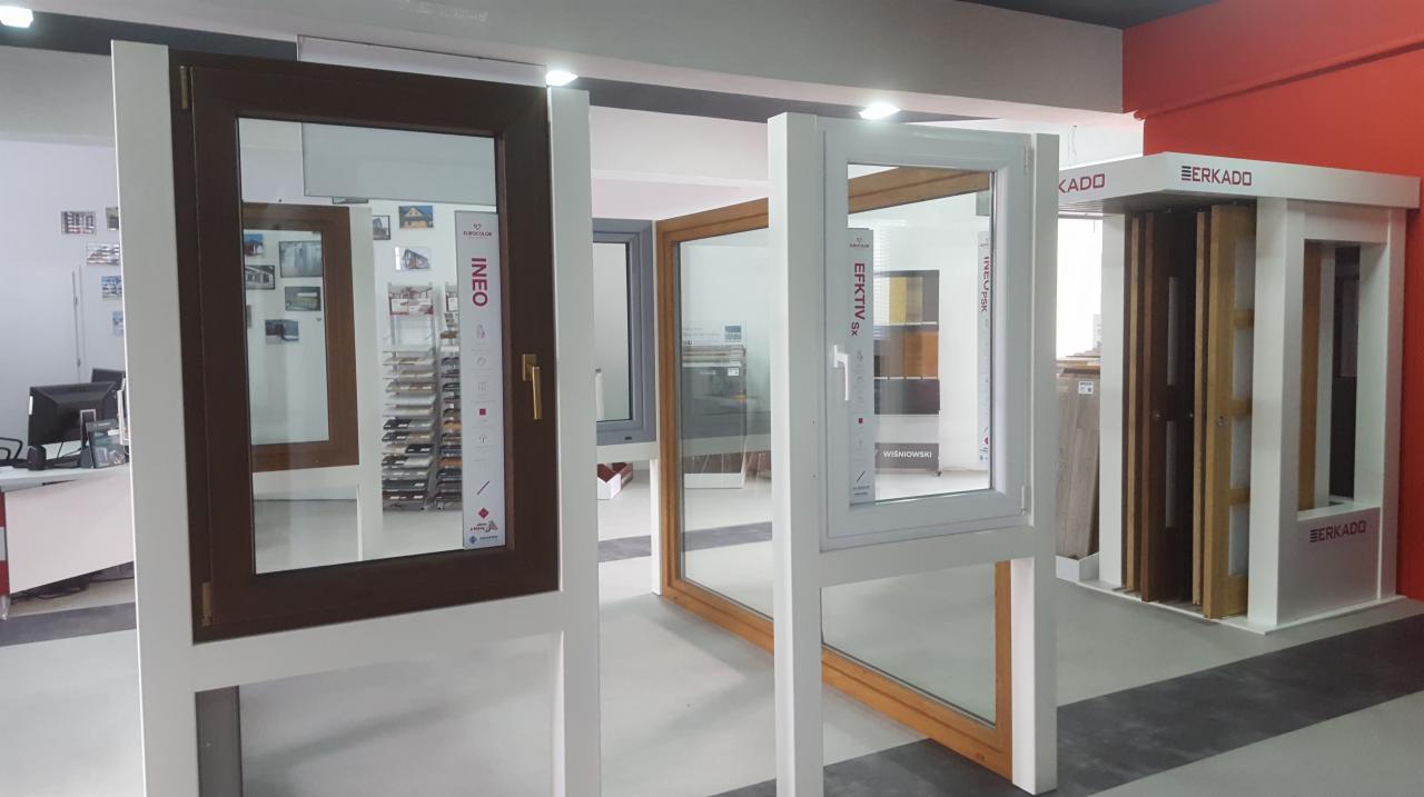 Ekspozycja w salonie sprzedaży: okna z profili INEO i EFEKTIV Sx na białych stojakach, w tle wzorniki kolorów i logo BERKADO, EMKAT Radomsko.