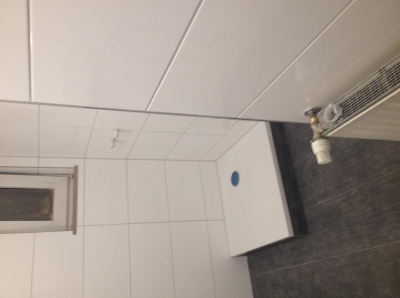 Białe, błyszczące płytki w łazience z minimalistycznym wyposażeniem, widok z góry. Uwagę zwraca nietypowe ułożenie płytek na suficie i ścianach.