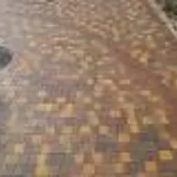 Ciepła kolorystyka kostki brukowej w jesiennym odcieniu, układana w parkowym stylu. Widoczny fragment studzienki kanalizacyjnej.