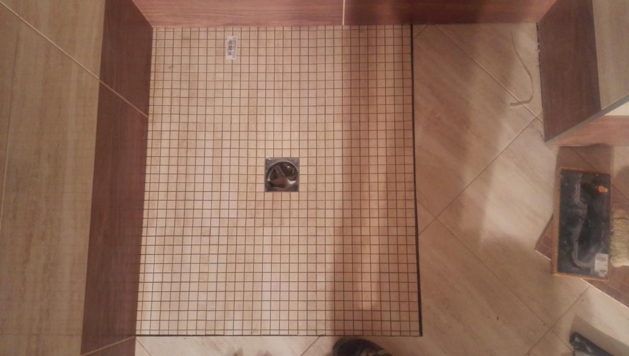 Brodzik z odpływem liniowym, przygotowany do układania płytek. Widoczne narzędzia glazurnicze. Beżowa kolorystyka, kwadratowa siatka na podłożu.