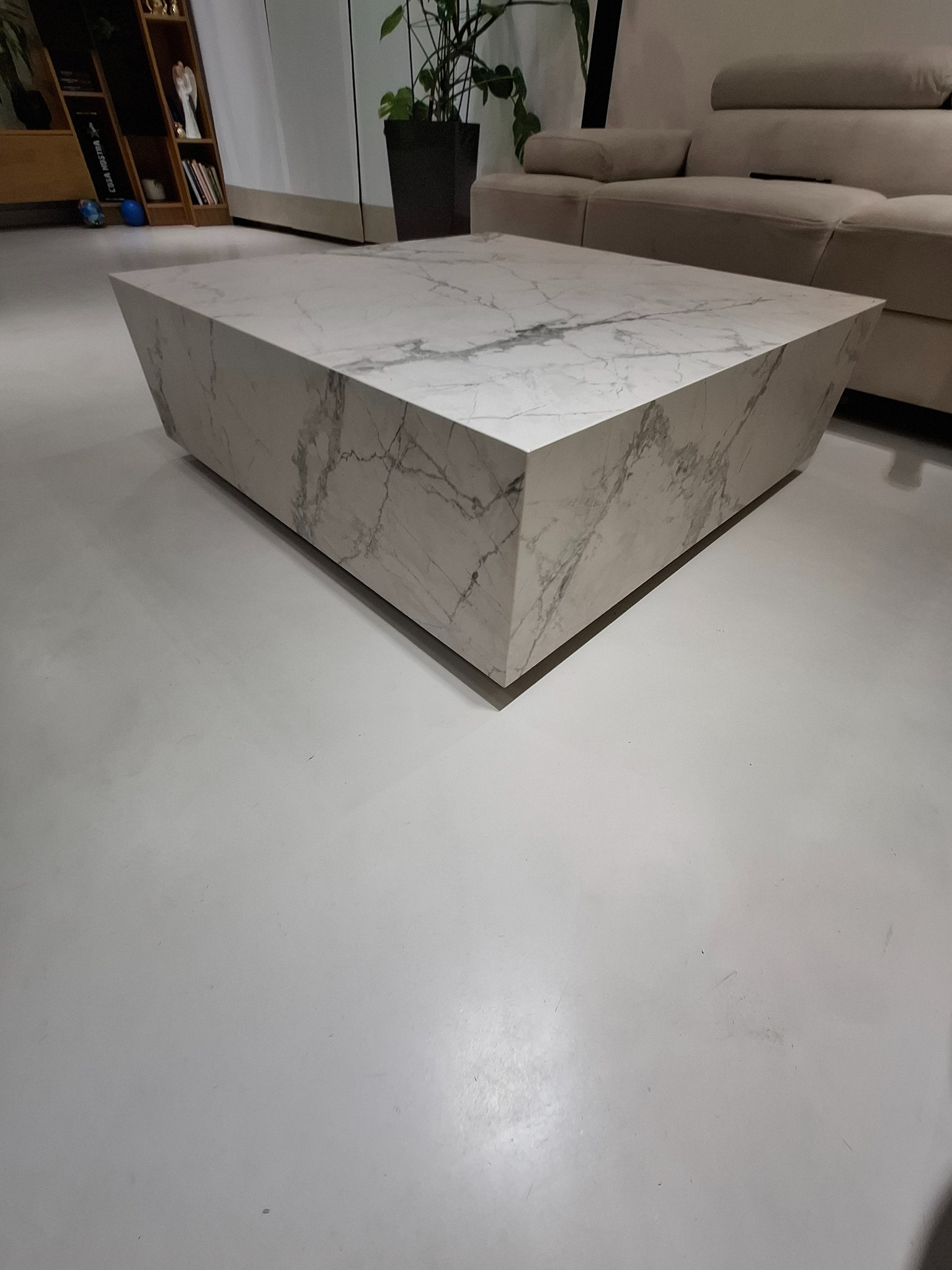 Minimalistyczny salon z kwadratowym stolikiem kawowym imitującym marmur, na tle beżowej sofy i jasnej podłogi. Nowoczesne wykończenie wnętrza.