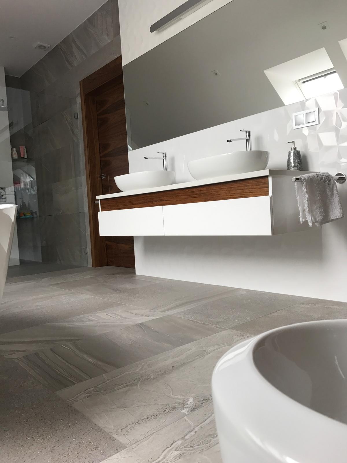 Nowoczesna łazienka z podwójną umywalką nablatową, drewnianym blatem i szarą, marmurkową podłogą. Minimalistyczny design, duże lustro i oświetlenie LED.