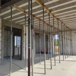 Wnętrze surowego domu z bloczków, widoczne szalunki stropowe podparte metalowymi stemplami, przygotowanie do wylania stropu.