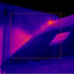 Termowizyjne zdjęcie budynku z zaznaczonymi obszarami w czerwonych i niebieskich ramkach, prezentujące rozkład temperatur w odcieniach fioletu, pomarańczy i żółci, z legendą temperatury po prawej...